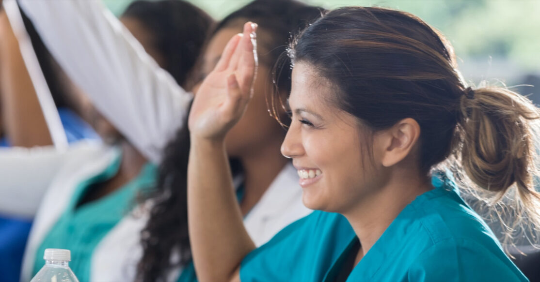 Lady in scrubs raising her hand at a training seminar
